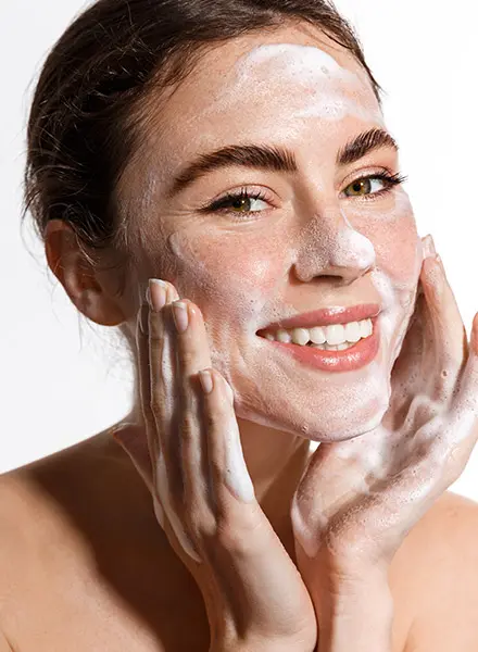 a smiling woman massages a skin cleansing foam on her face
