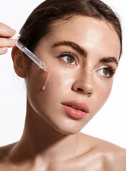 a woman applies an transparent liquid on her cheek with a pipette