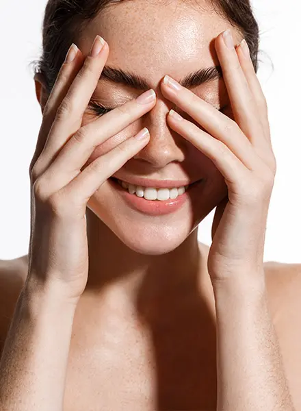 a smiling woman hides her eyes behind her hands